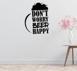 a wall decal with the text "DON'T WORRY BEER HAPPY" in a bold, black font. The wall is plain white, and there is a small table with a vase of pink flowers in the foreground.