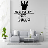 a wall with a humorous text sticker that reads "MY BUCKET LIST: ICE BEER" along with a bucket icon. Below the sticker, there is a list of items, including "ICE" and "BEER", indicating a bucket list of drinks. The room has a gray couch, a coffee table, and a potted plant, creating a cozy and inviting atmosphere.