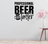 a wall decal with the text "PROFESSIONAL BEER TASTER" in a bold, black font. Below the text, there is a graphic of a beer mug. The wall decal is set against a white wall, and there is a small table with a vase of pink flowers to the right of the decal.