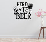 a wall with a black and white text sticker that says "HERE for the BEER" along with a beer mug icon. Next to the sticker, there is a small table with a vase of pink flowers.