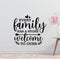 a wall with a black and white text quote that reads "Every family has a story welcome to ours" and a small vase with pink flowers placed next to it.