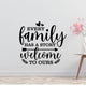 a wall with a black and white text quote that reads "Every family has a story welcome to ours" and a small vase with pink flowers placed next to it.