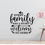 a wall with a black and white text quote that reads "Every family has a story welcome to ours" and a small vase with pink flowers placed next to it.