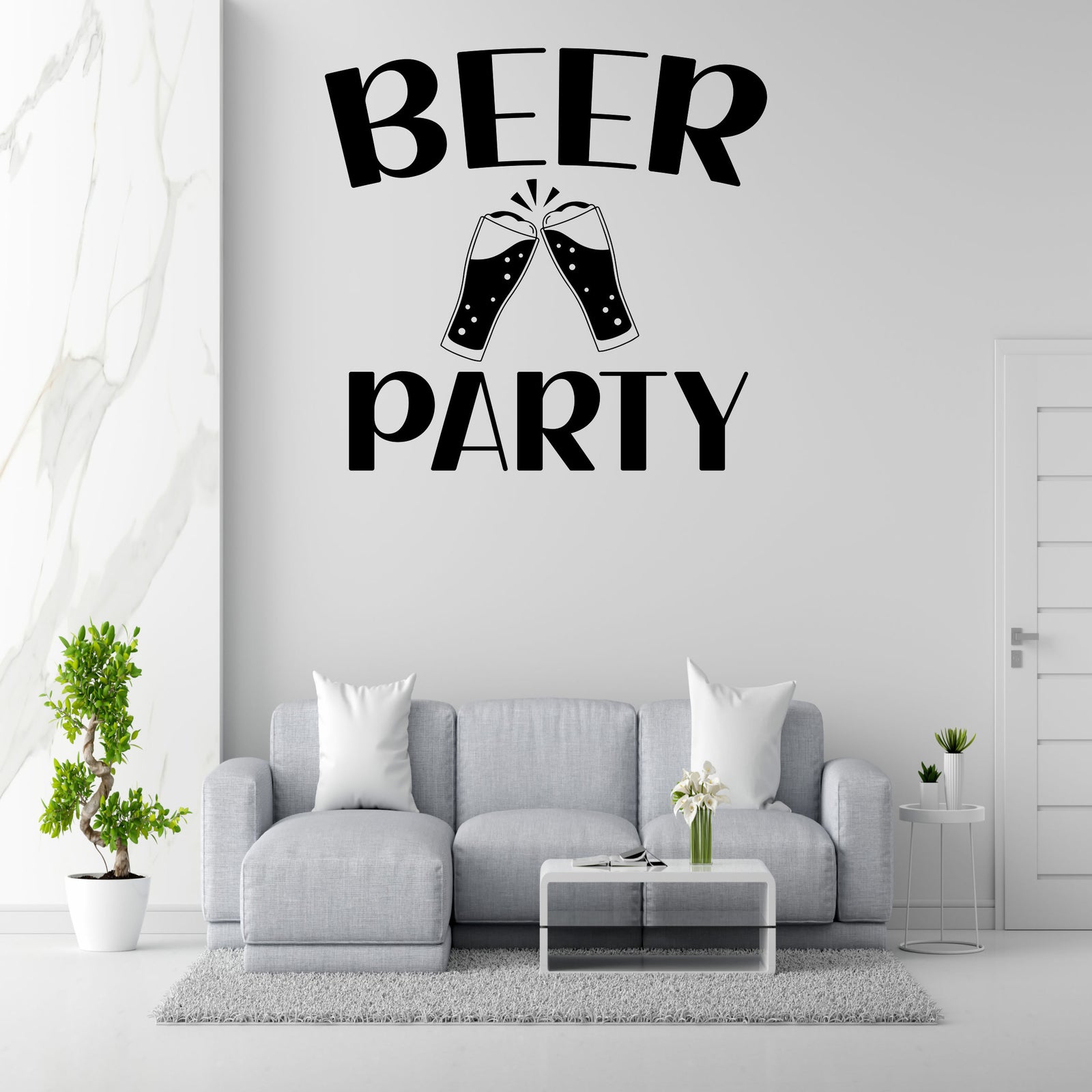 a living room with a gray sofa, a coffee table, and a potted plant. Above the sofa, there is a large wall decal that says 