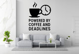 a living room with a gray sofa, a coffee table, and a potted plant. Above the sofa, there is a wall decal that says "POWERED BY COFFEE AND DEADLINES".