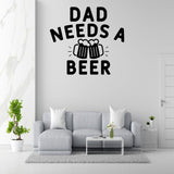 a living room with a gray sofa, a coffee table, and a potted plant. Above the sofa, there is a wall decal that says "DAD NEEDS A BEER".