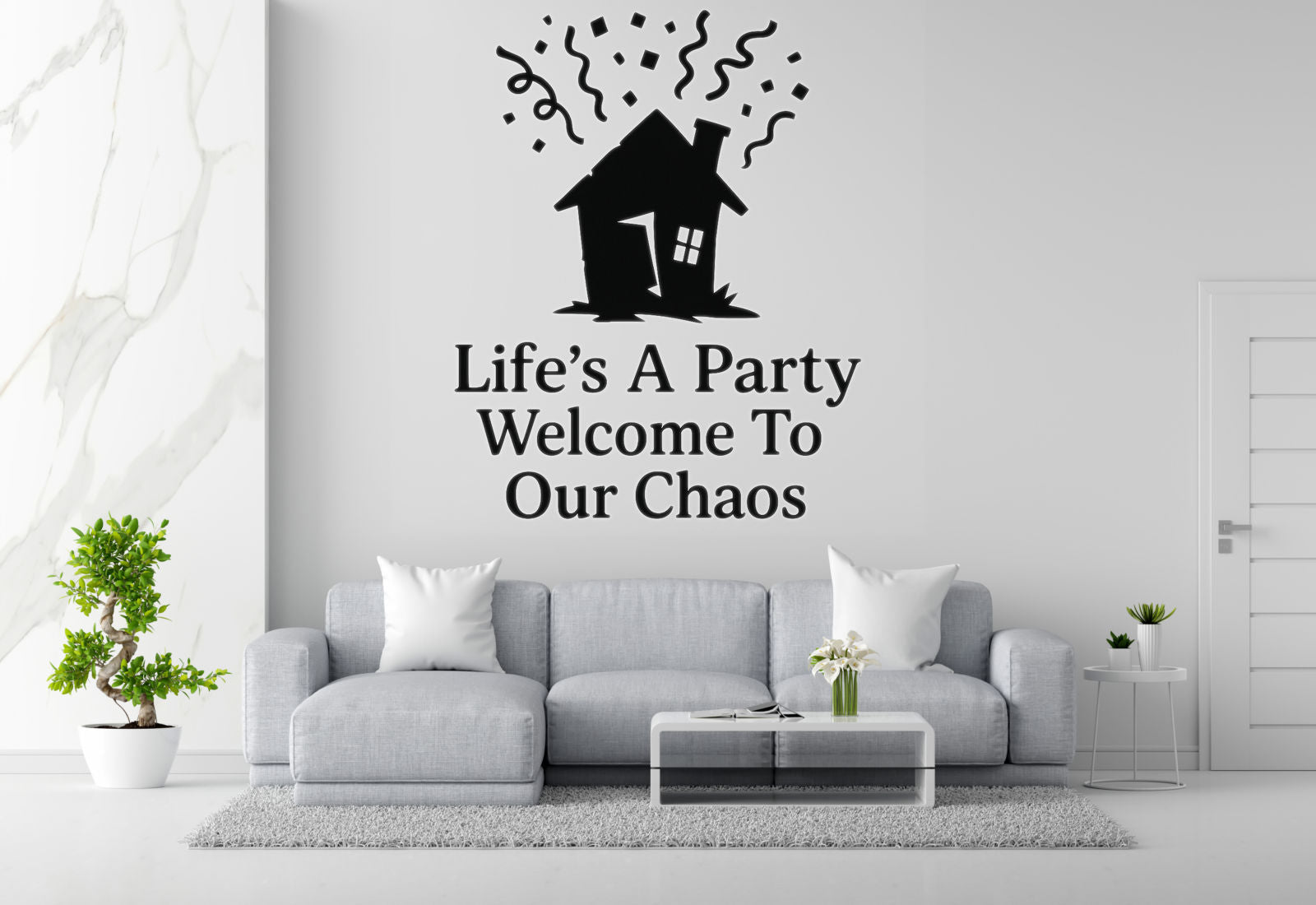 a living room with a gray sofa, a coffee table, and a potted plant. Above the sofa, there is a wall decal that says 