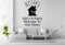 a living room with a gray sofa, a coffee table, and a potted plant. Above the sofa, there is a wall decal that says "Life's A Party Welcome To Our Chaos".