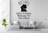 a living room with a gray sofa, a coffee table, and a potted plant. Above the sofa, there is a wall decal that says "Life's A Party Welcome To Our Chaos".