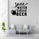 a living room with a gray sofa, a coffee table, and a potted plant. Above the sofa, there is a wall decal that says "Save Water, Drink Beer".