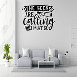 a wall decal with the text "THE BEERS ARE CALLING I MUST GO" in a modern living room setting with a gray sofa, a coffee table, and a potted plant.