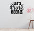 a wall with a black and white text design that says "LET'S DRINK BEER" along with a beer mug icon. Next to the wall, there is a wooden table with a vase of pink flowers on it.