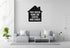 a living room with a gray sofa, a coffee table, and a potted plant. Above the sofa, there is a black and white sign that reads "This house runs on coffee and chaos".