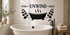 SOAK UNWIND RESET black vinyl bathroom wall decal with bathtub, steam, and eucalyptus above a white freestanding tub.