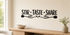 Black Stir Taste Share kitchen wall decal with spoon and herb flourishes above a light wood console on a smooth cream wall.