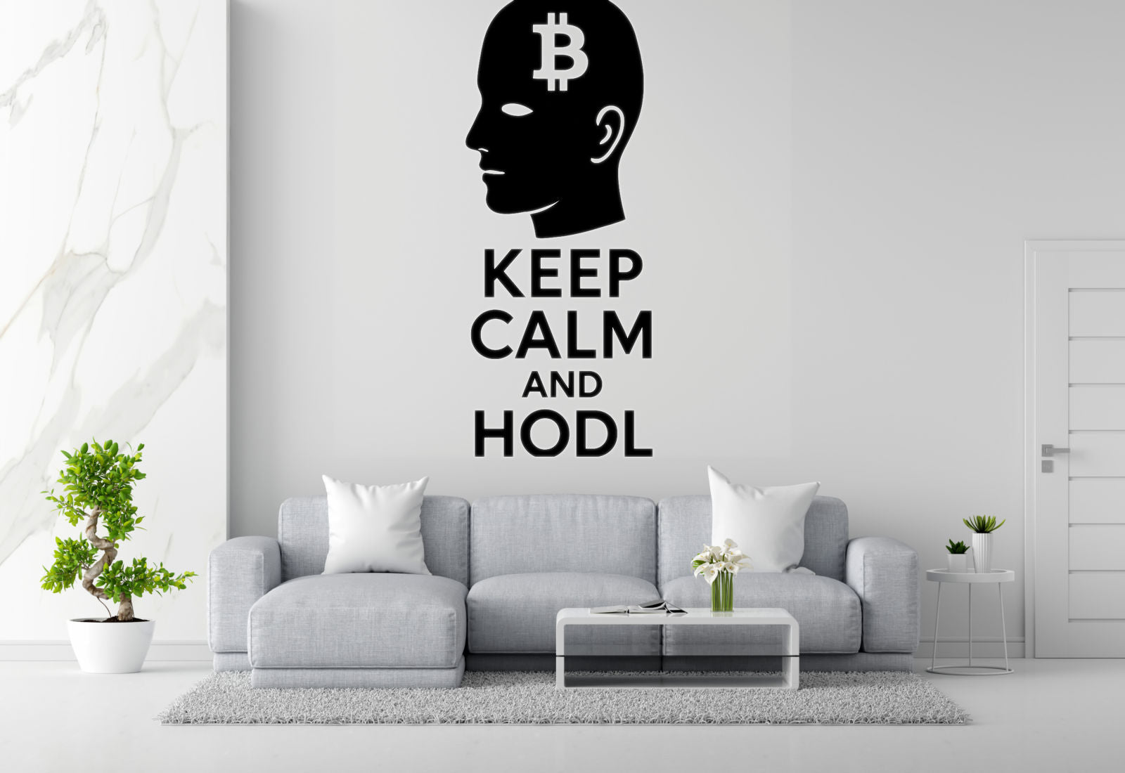 a living room with a gray sofa, a coffee table, and a potted plant. Above the sofa, there is a wall decal with the text "KEEP CALM AND HODL" in black letters.