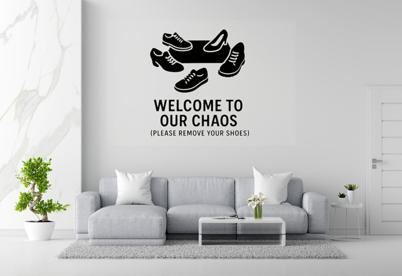 a living room with a gray sofa, a coffee table, and a potted plant. Above the sofa, there is a wall decal that says 