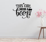 a wall decal with the text "THIS GIRL NEEDS A BEER" in a stylized font, accompanied by a beer mug icon. The wall is plain white, and there is a small table with a vase of pink flowers to the right of the decal.