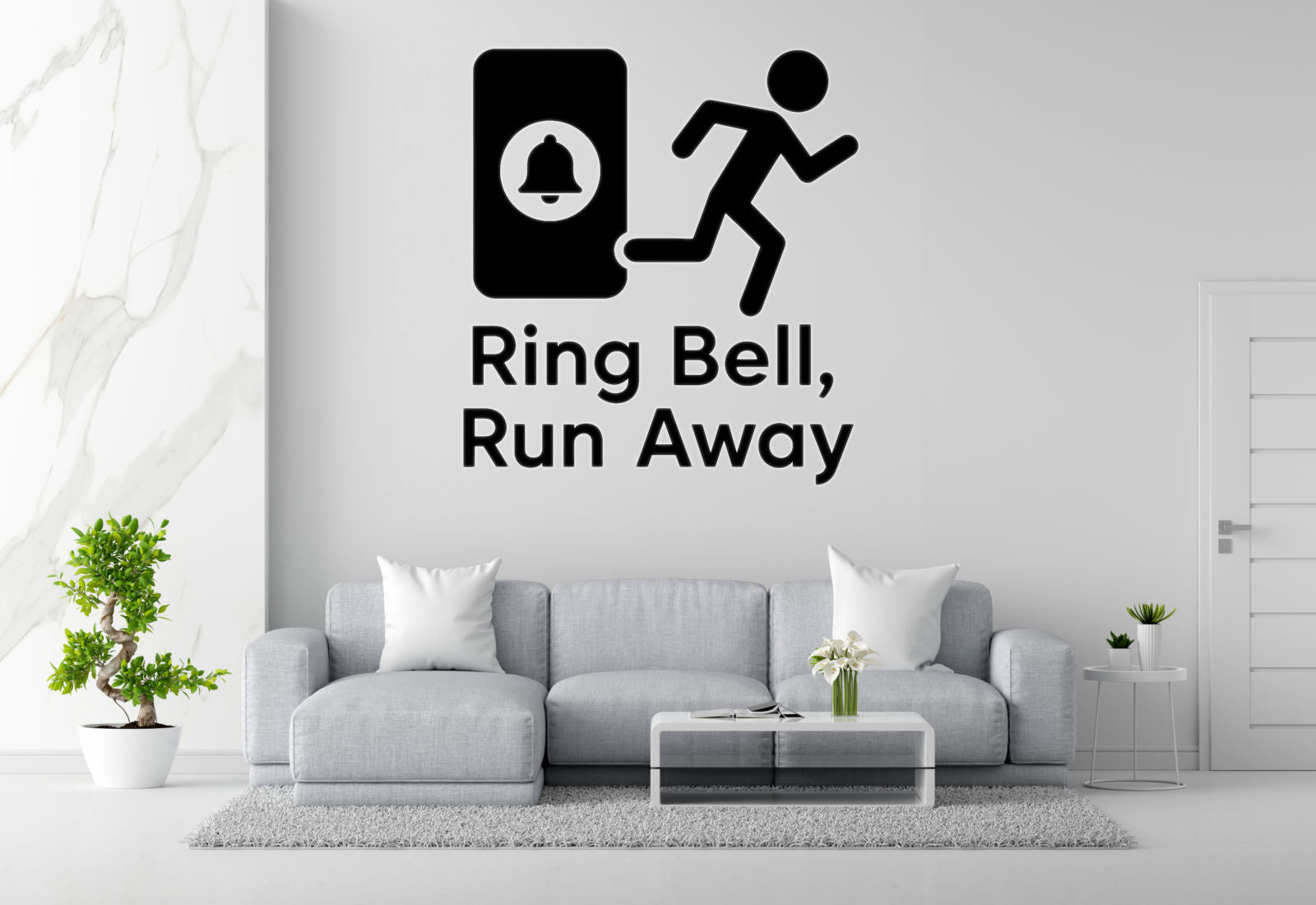 a living room with a gray sofa, a coffee table, and a potted plant. Above the sofa, there is a wall decal that says 