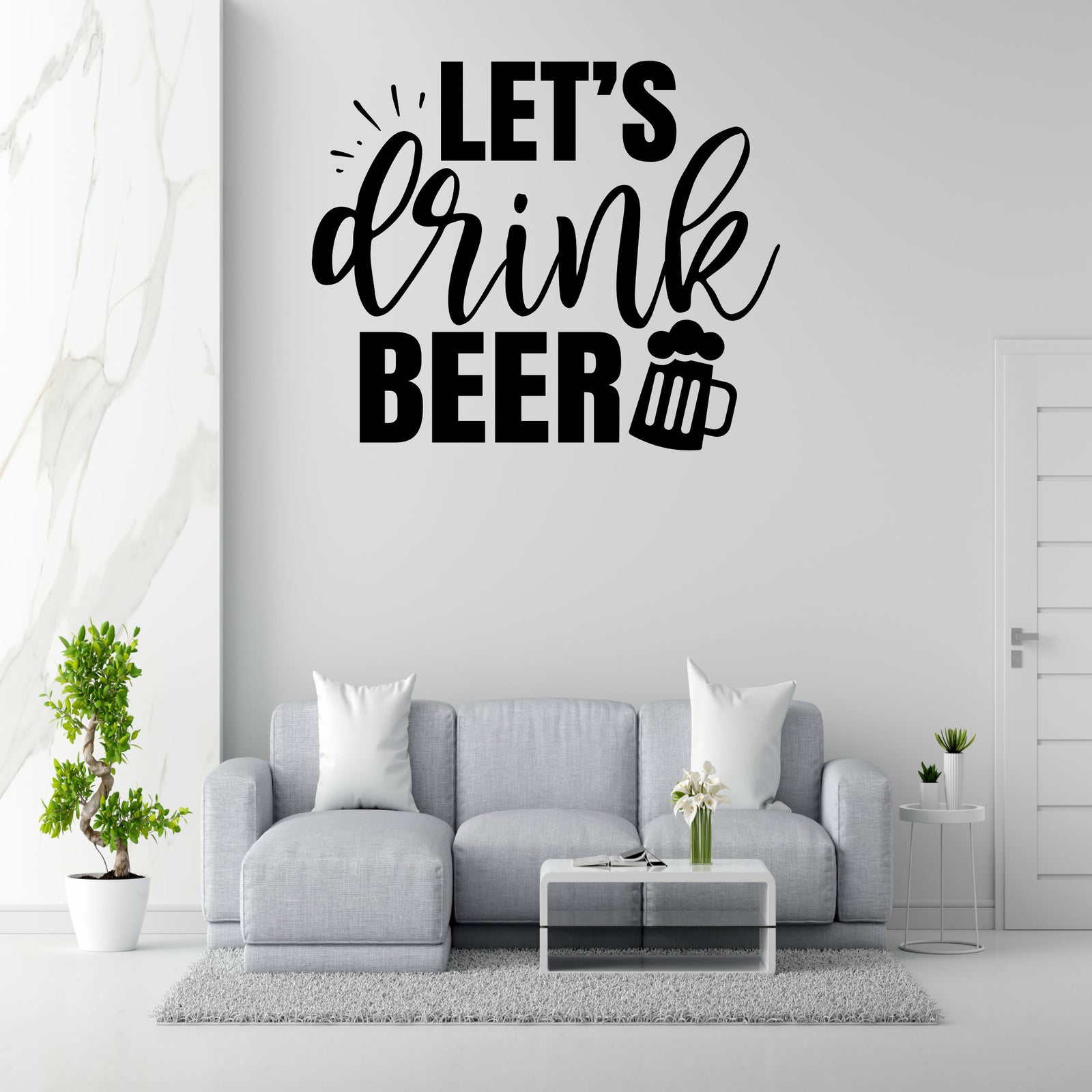 a living room with a gray sofa, a coffee table, and a potted plant. Above the sofa, there is a wall decoration that says 