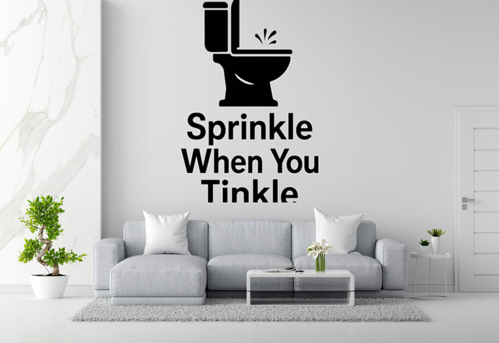 a living room with a gray sofa, a coffee table, and a potted plant. Above the sofa, there is a wall decal that says "Sprinkle When You Tinkle".