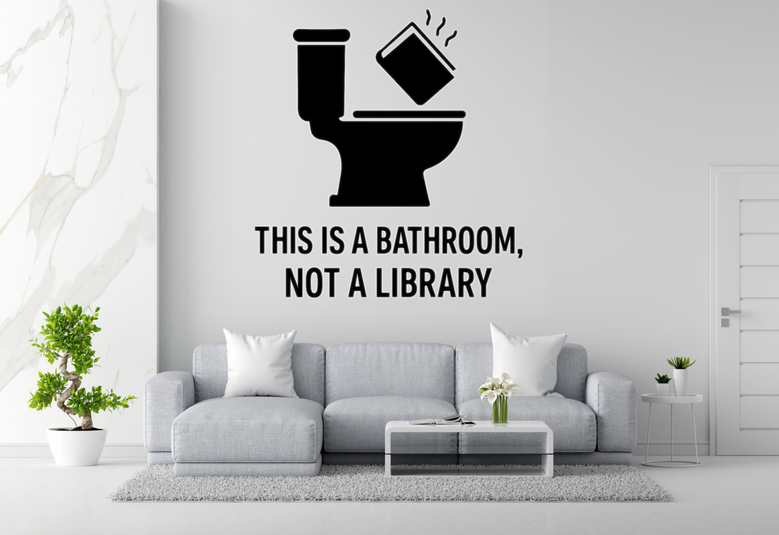 a living room with a gray sofa, a coffee table, and a potted plant. Above the sofa, there is a wall decal that reads "THIS IS A BATHROOM, NOT A LIBRARY".